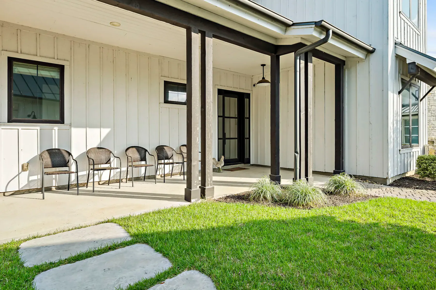 Covered patio with seating beside a glass door, lawn, and stepping stones.