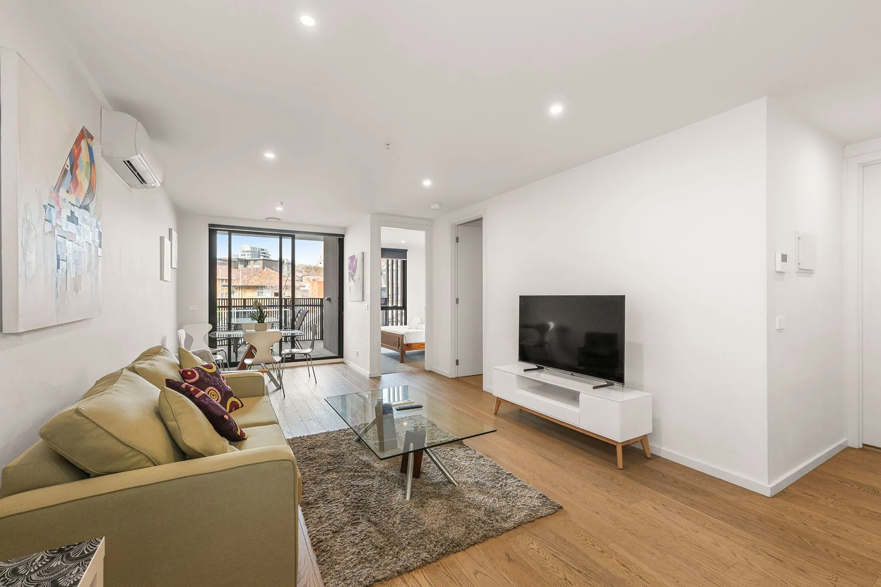 A bright living room with seating, a television, and glass doors to a balcony.