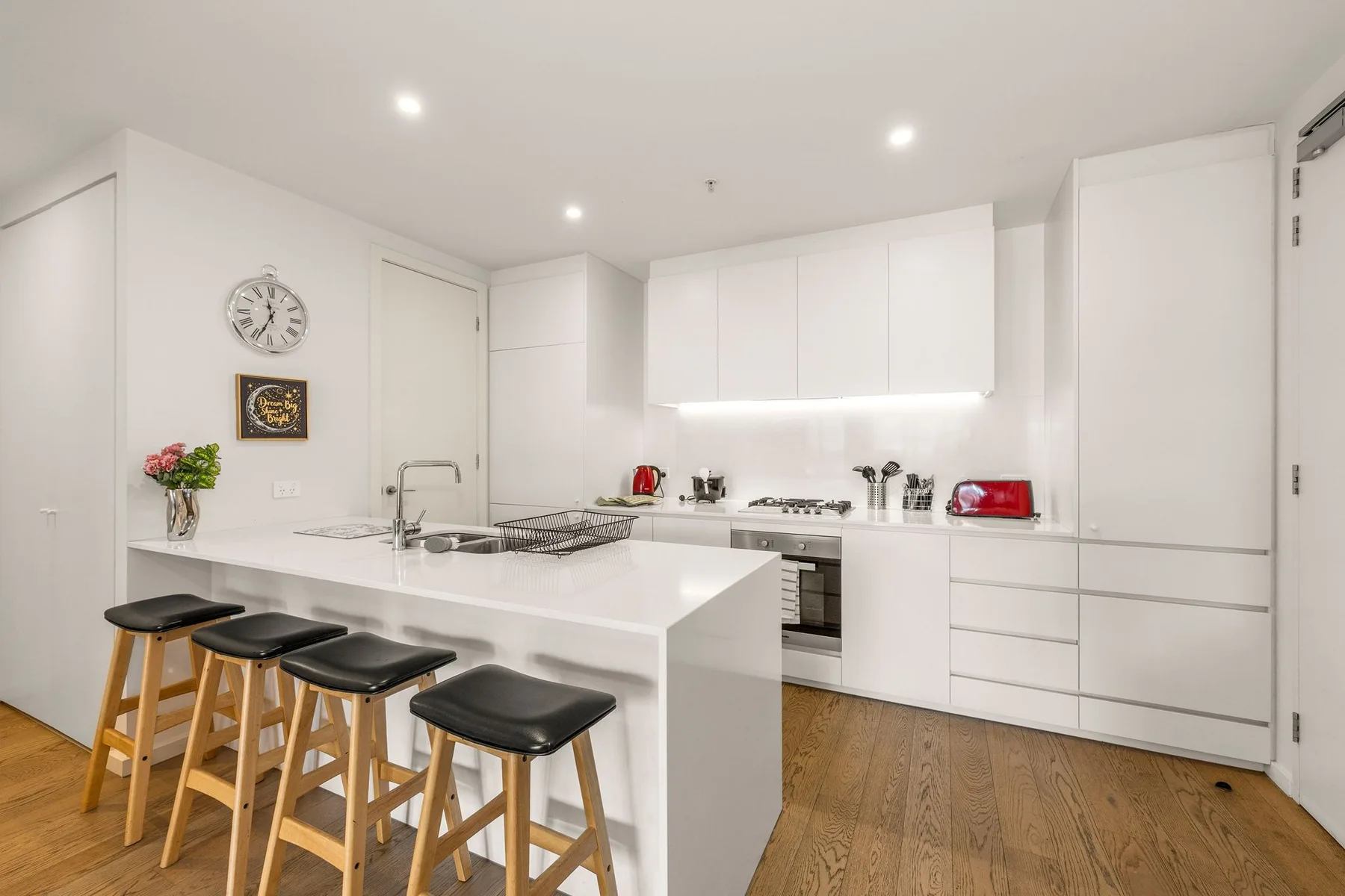 A bright white kitchen with a central island and wooden stools.