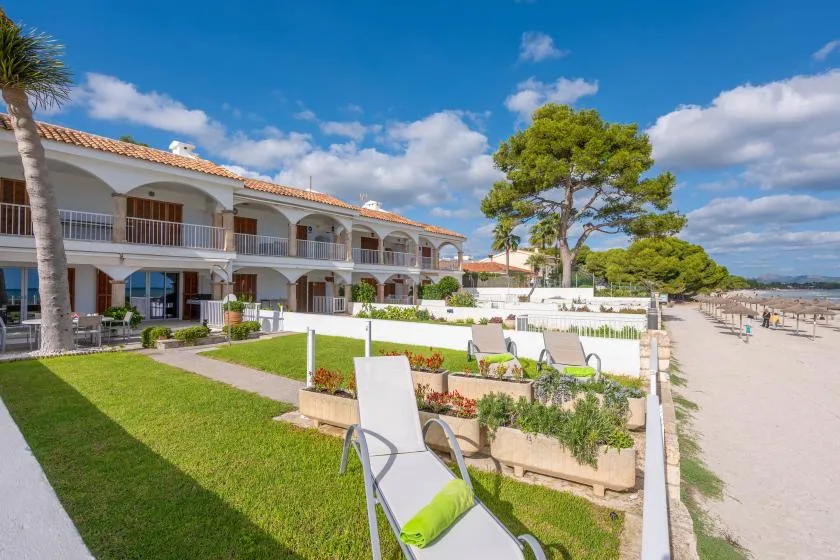 A beachfront resort building overlooks a sandy shore, with garden seating in front.