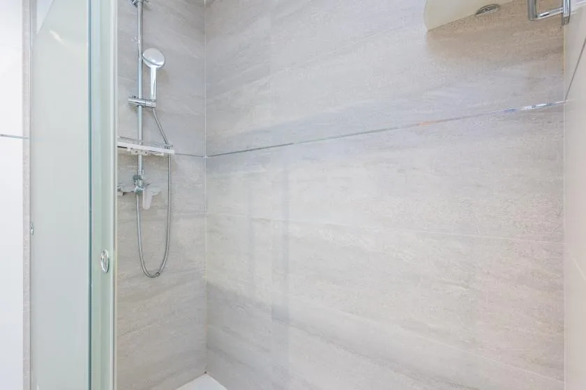A tiled shower with a handheld showerhead and glass panel.