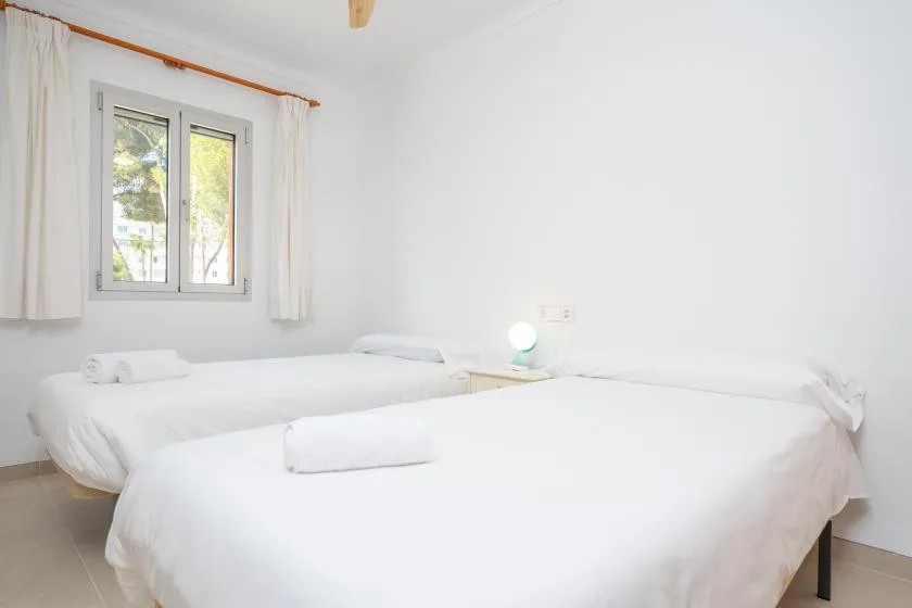 A bright bedroom with two beds, white bedding, and a window.