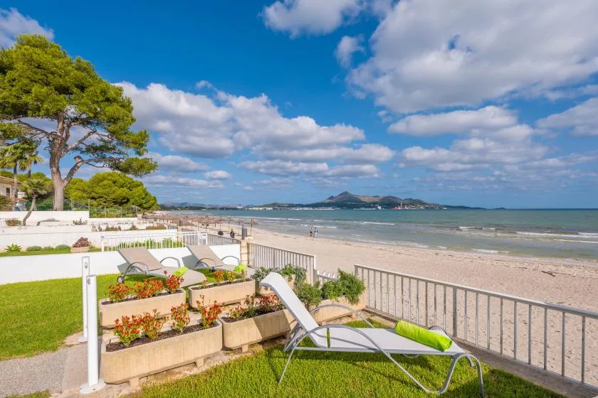 A seaside terrace with lounge seating overlooks a sandy beach and calm water.