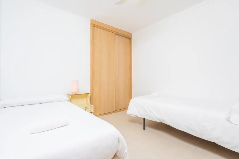 A bright bedroom with two beds and a wooden wardrobe.
