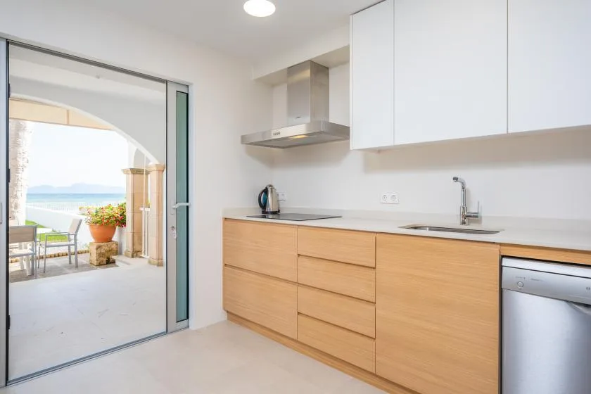 A modern kitchen with light wood cabinets and a sliding glass door opening onto a patio.
