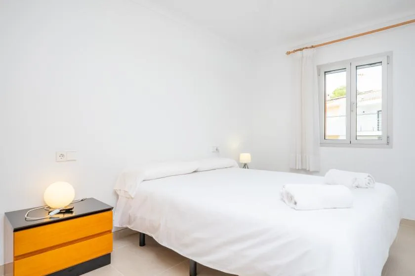 A bright bedroom with white bedding and a window beside the bed.