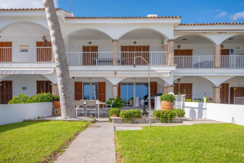 A white multi-unit building with arched balconies and a grassy front courtyard.