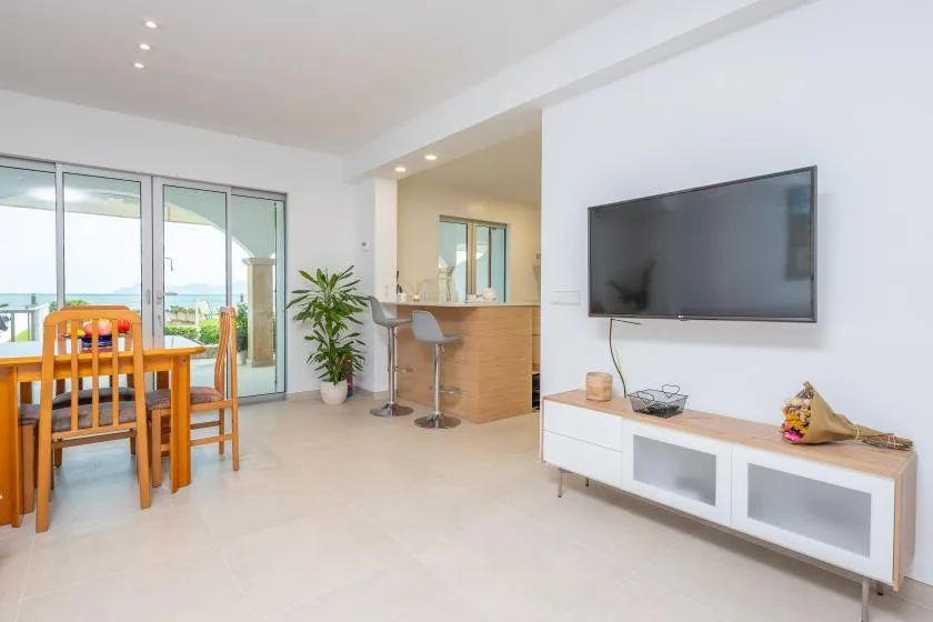 A bright open-plan living and dining area with a television and sliding glass doors.