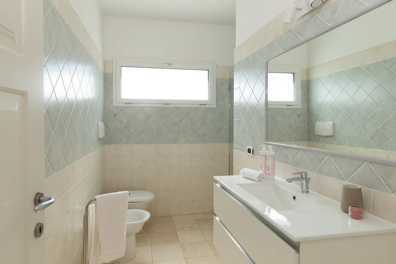 Un baño alicatado con lavabo, inodoro y una ventana alta.