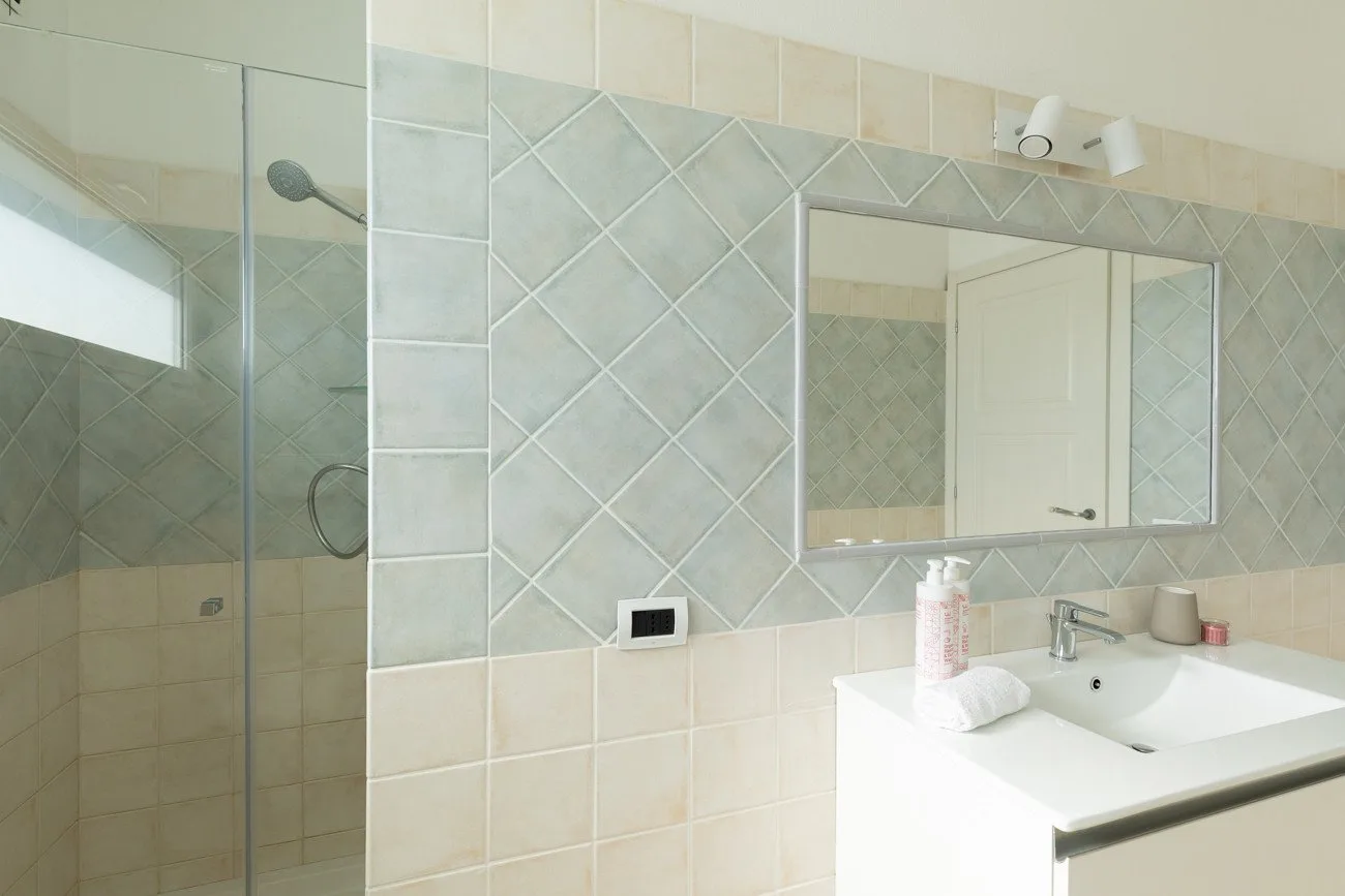 Un baño alicatado con una ducha de vidrio y un lavabo bajo un espejo.