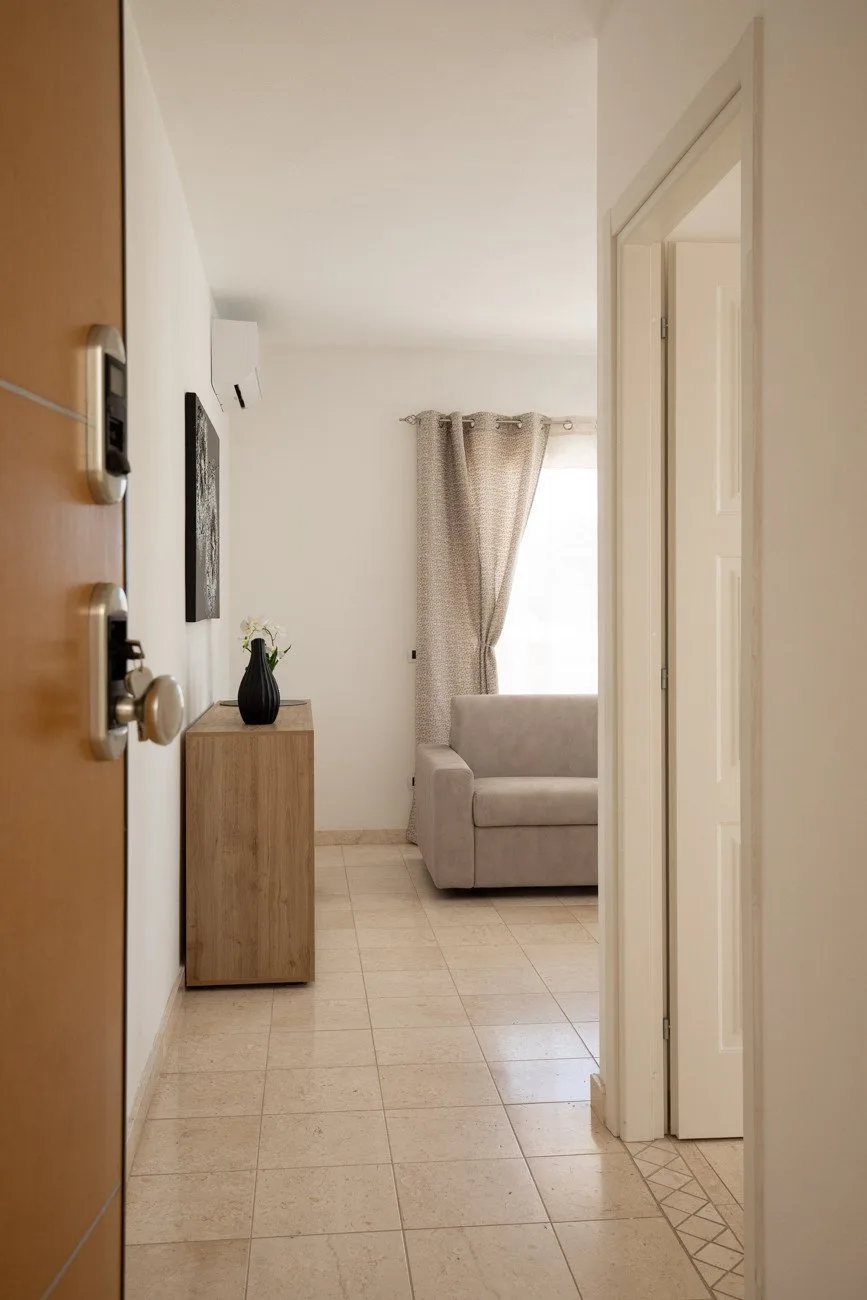 Un pasillo con suelo de baldosas da a una sala de estar con asientos junto a una ventana con cortinas.