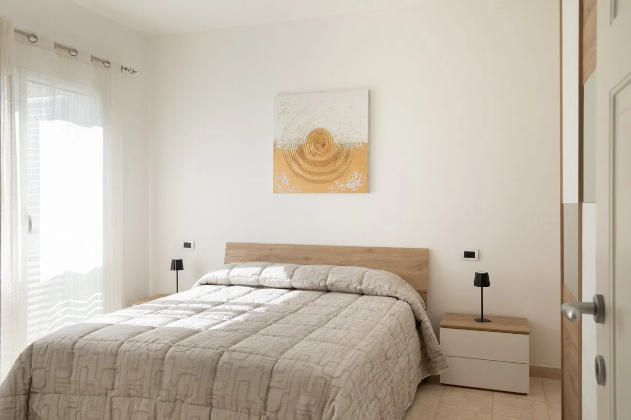 Un dormitorio con una cama tendida, mesitas de noche y arte abstracto en la pared.