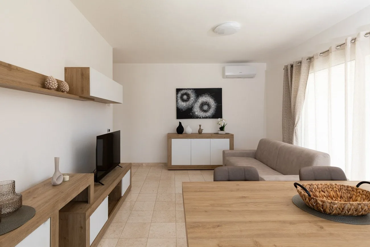 Una sala de estar con televisor, asientos y una mesa de centro de madera.