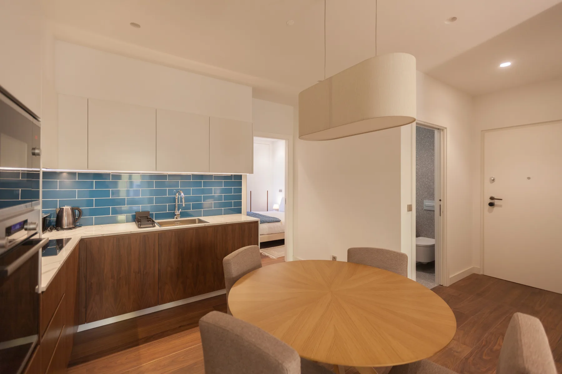 A modern kitchen and dining area with blue tile backsplash and a round table.