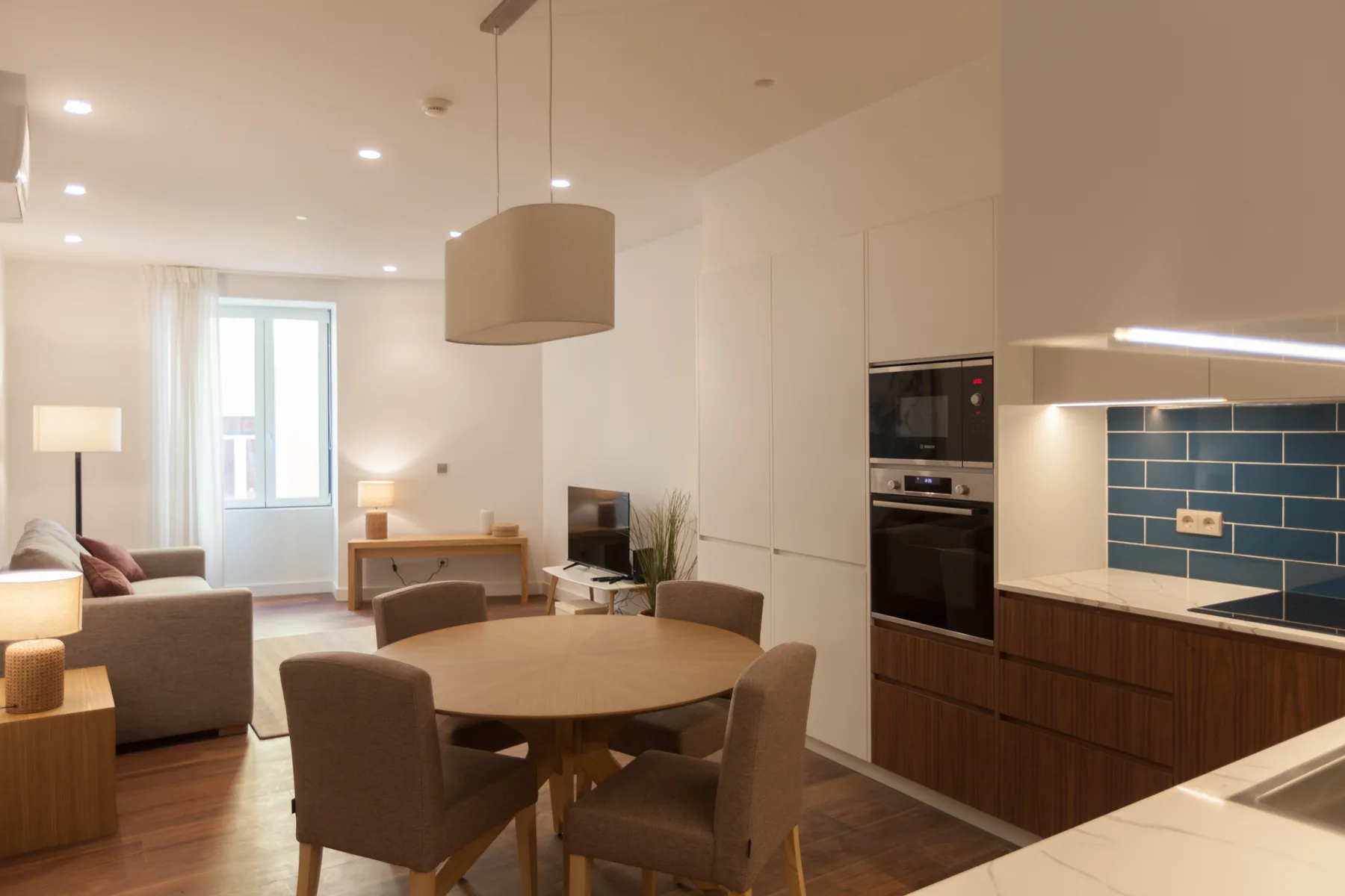 A bright open-plan living and dining area with a kitchen and blue tile backsplash.
