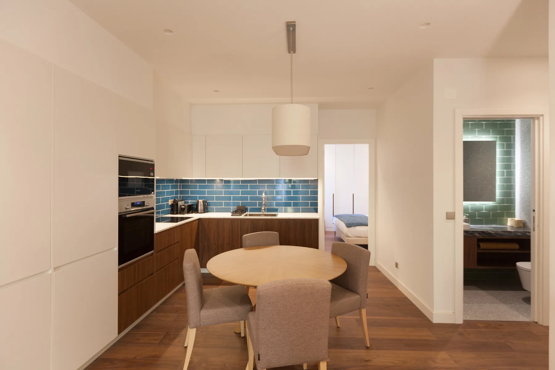 A dining area with a round table beside a kitchen with blue tile backsplash.
