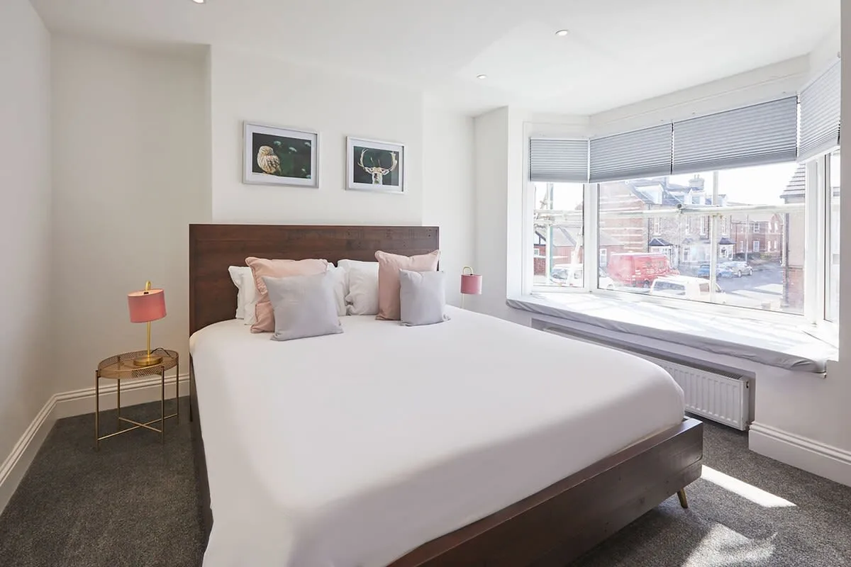 A bright bedroom with a neatly made bed beside a large window.