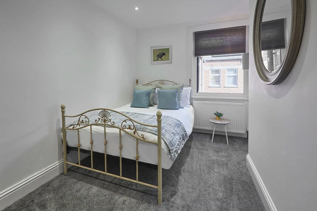 A bedroom with a brass bed, gray carpet, and a window.