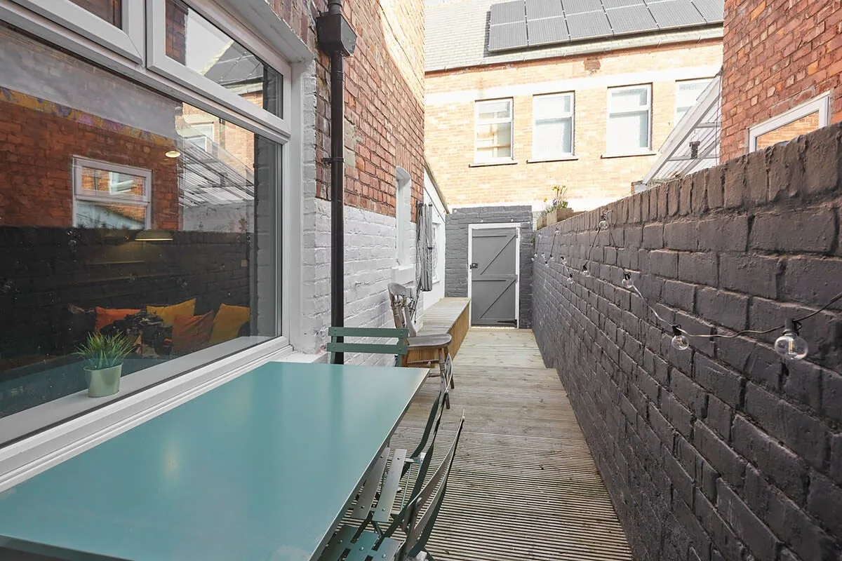 A narrow outdoor patio with a table and seating beside brick walls.