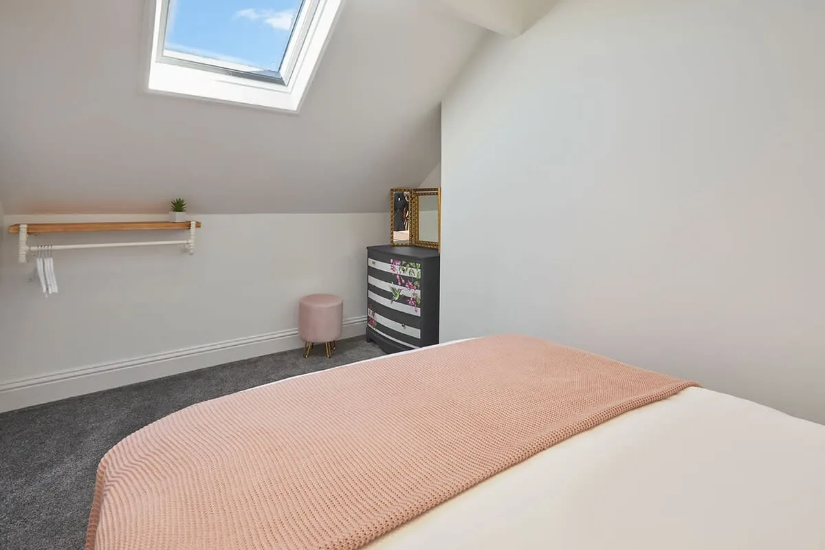 A bright bedroom with a bed beneath a sloped ceiling and skylight.