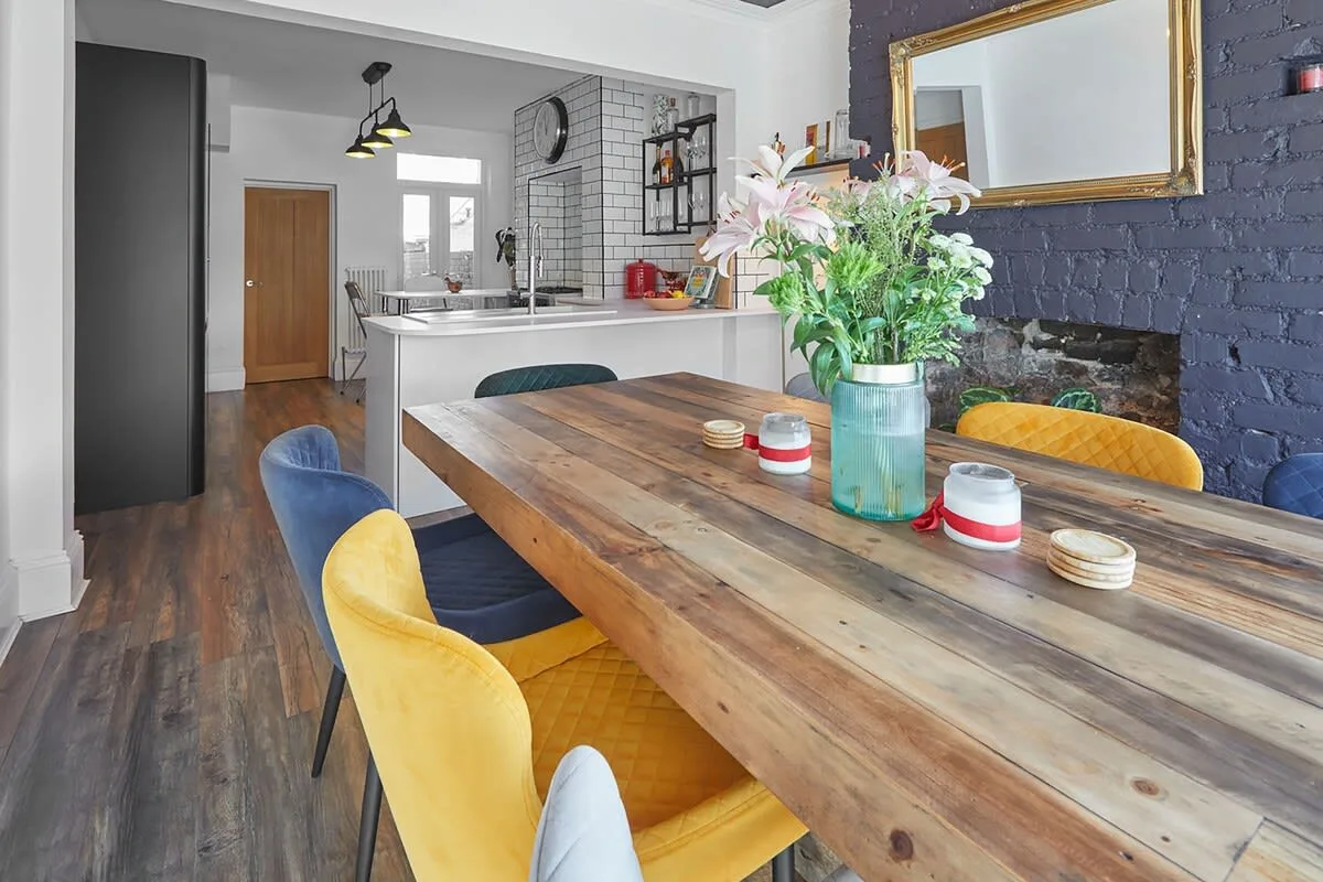 A dining area with a long wooden table and colorful chairs beside the kitchen.