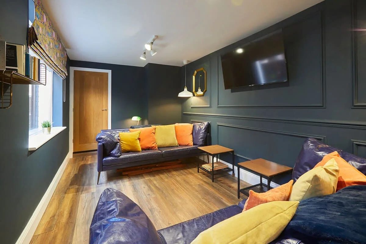 A dark-walled living room with seating, a coffee table, and a wall-mounted television.