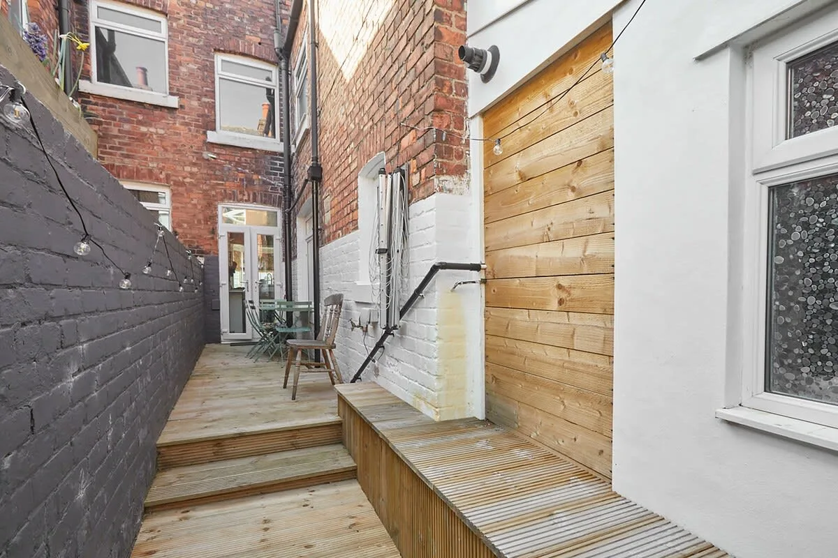 A narrow outdoor patio with wooden decking, steps, and a table with chairs.