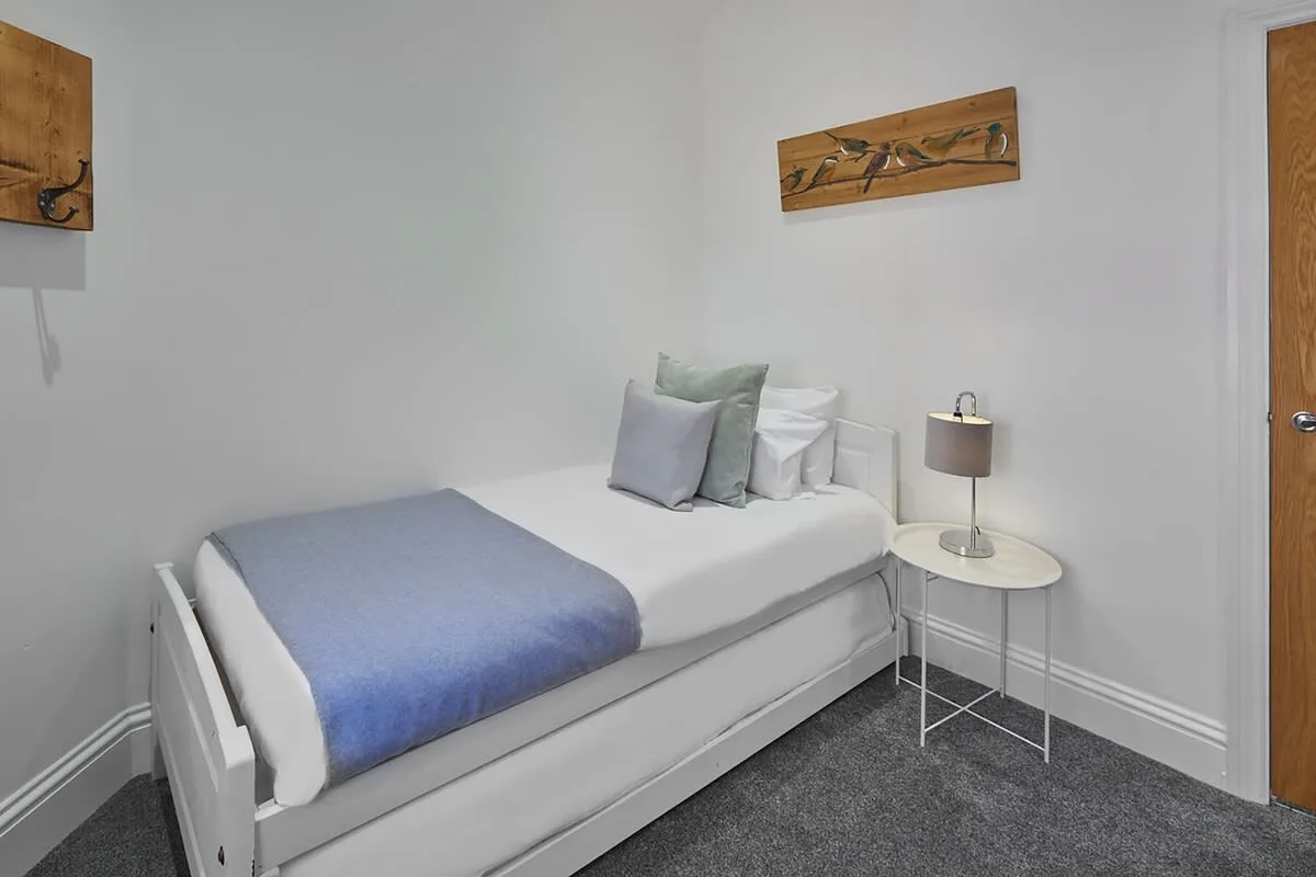 A single bed with white bedding and a blue blanket sits in a compact bedroom.