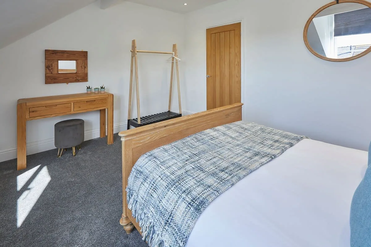 A bedroom with a bed, wooden desk, and freestanding clothes rack.