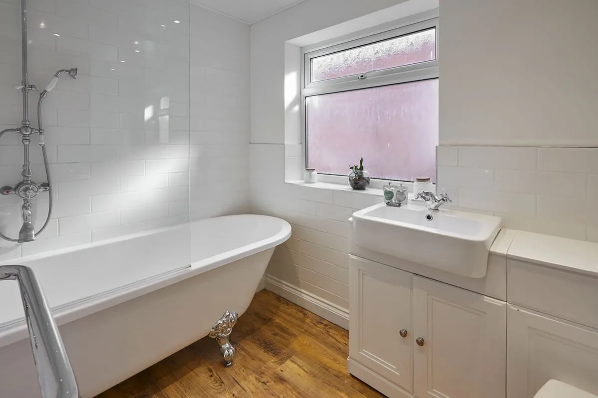 A bathroom with a bathtub, shower, and sink beneath a window.