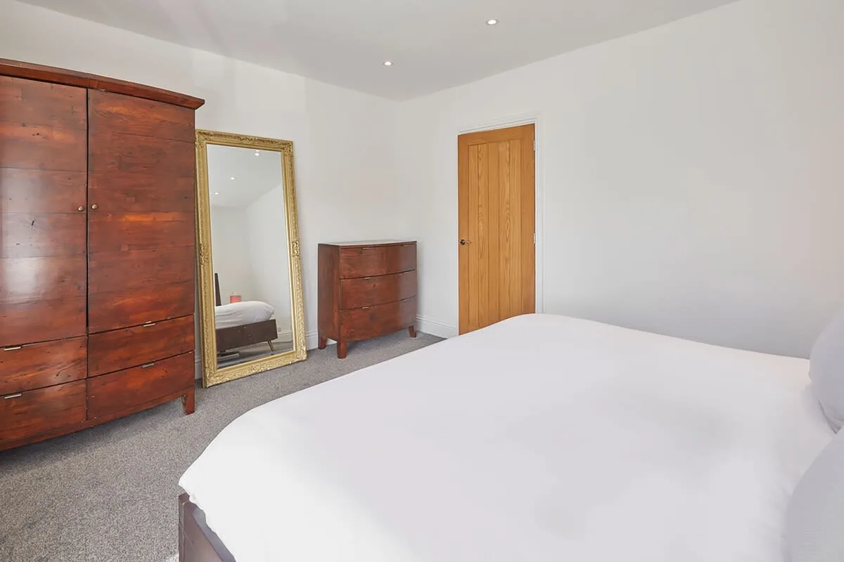 A bedroom with a bed, wooden wardrobes, and a full-length mirror.