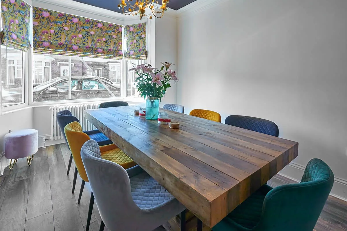 A dining room with a long wooden table and colorful seating.