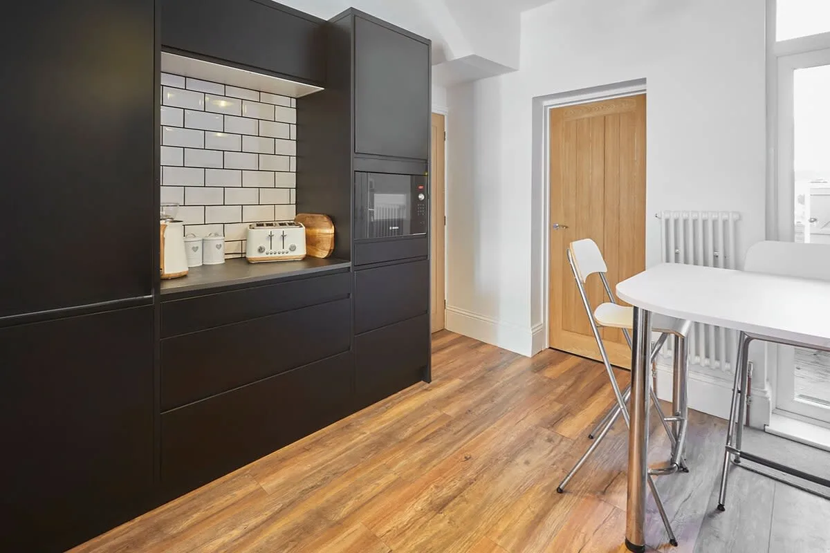 A compact kitchen area with dark cabinetry, a tiled backsplash, and a small table.