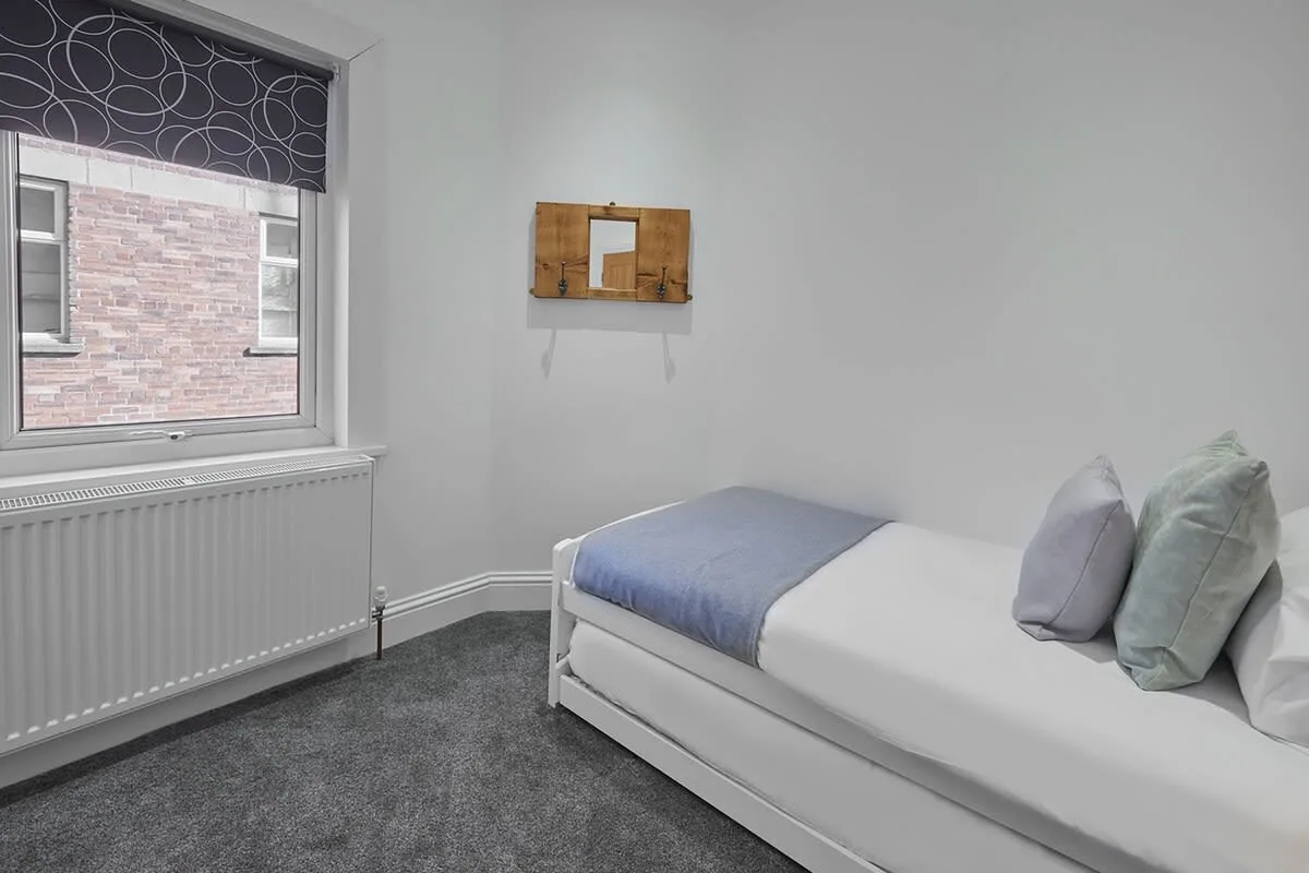 A bedroom with a single bed, a window, and a radiator.