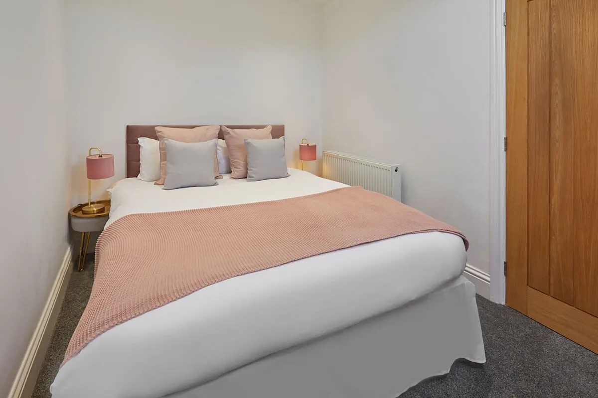 A bedroom with a neatly made bed and pink bedding.