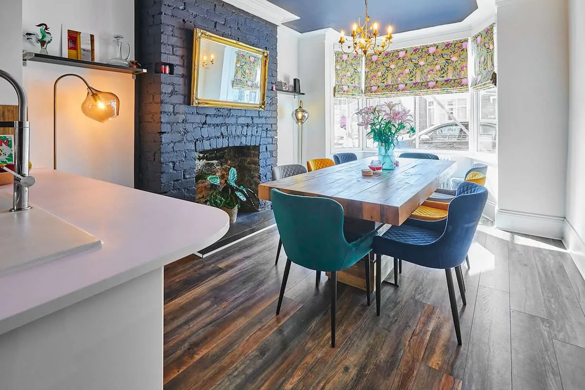 A dining area with a wooden table and colorful seating beside a bright window.