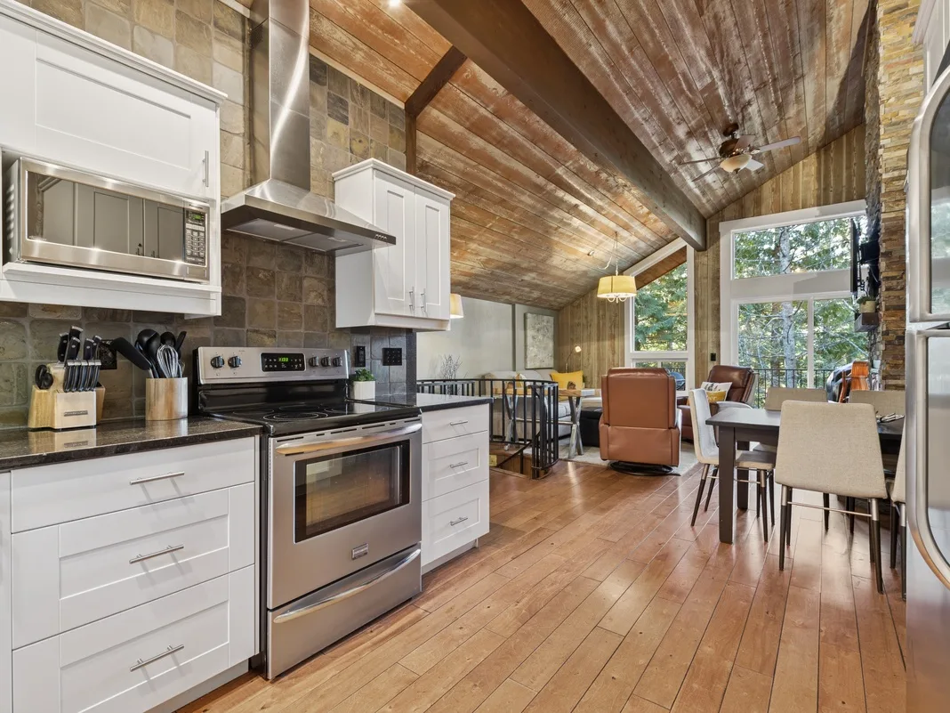Gather around this stunning open-concept kitchen where exposed wooden beams create rustic charm above modern appliances and white cabinetry.
