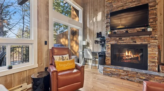 A living room with a leather chair beside a lit fireplace and large windows.