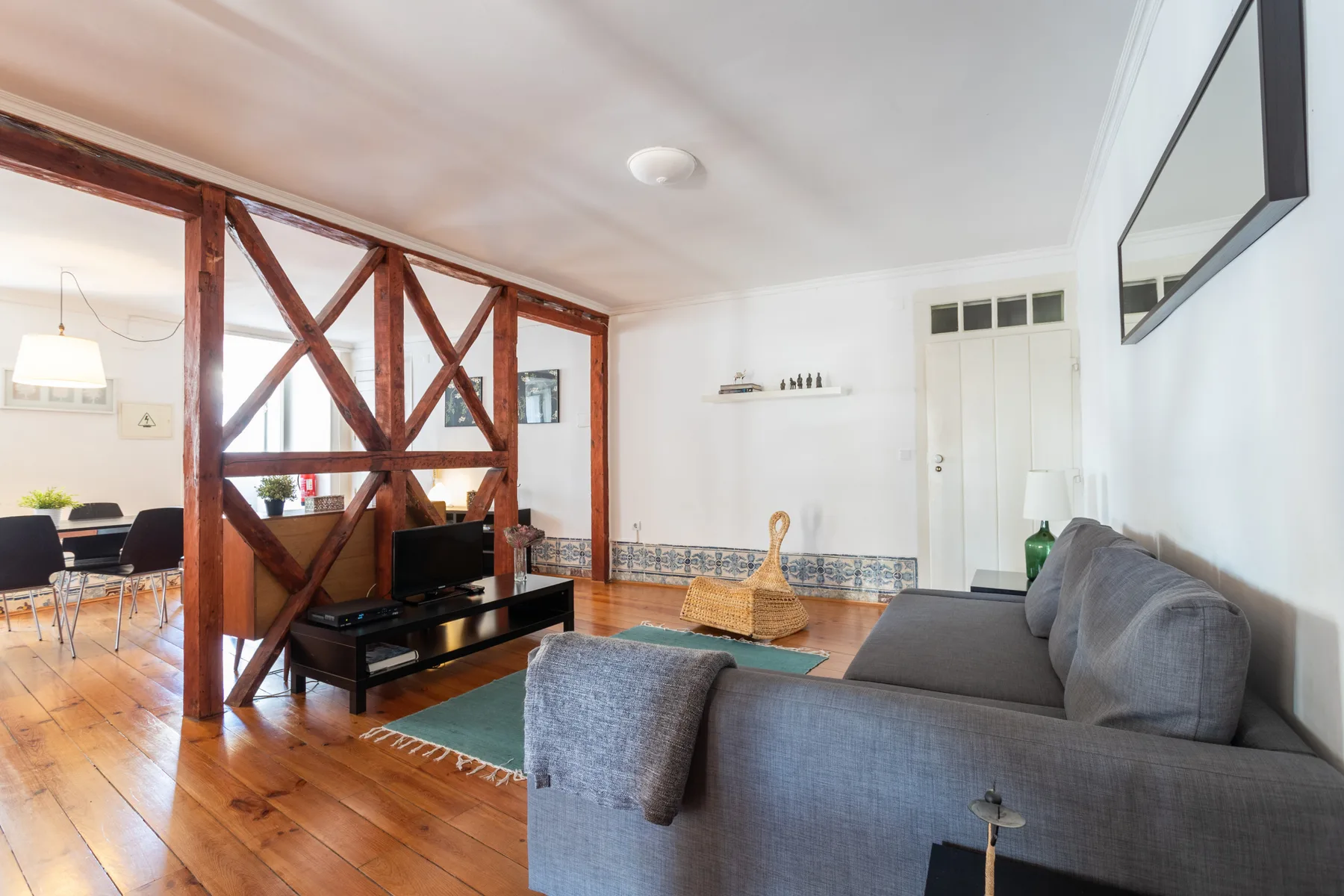 Sala de estar con asientos grises, un televisor y vigas de madera a la vista.