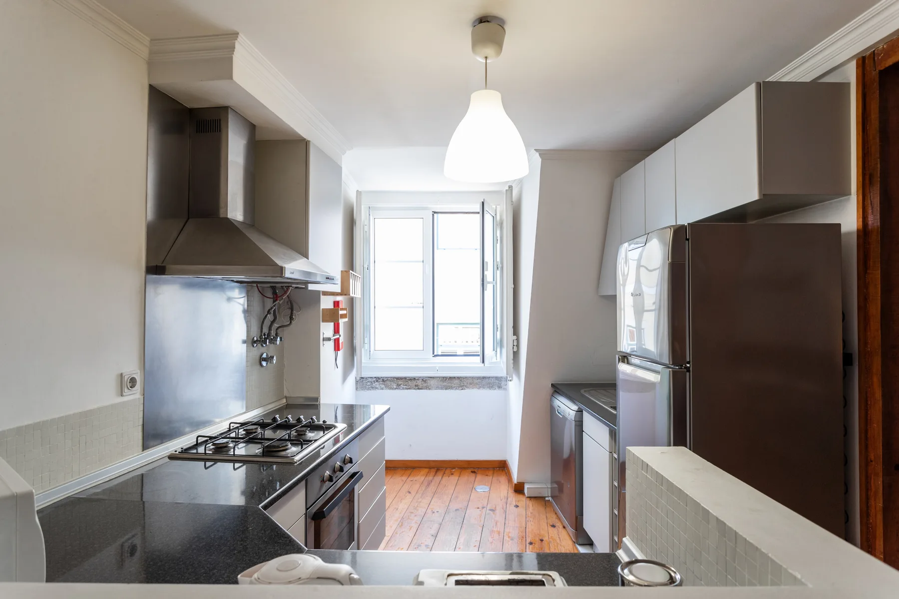 Una cocina luminosa con una ventana central y suelo de madera.