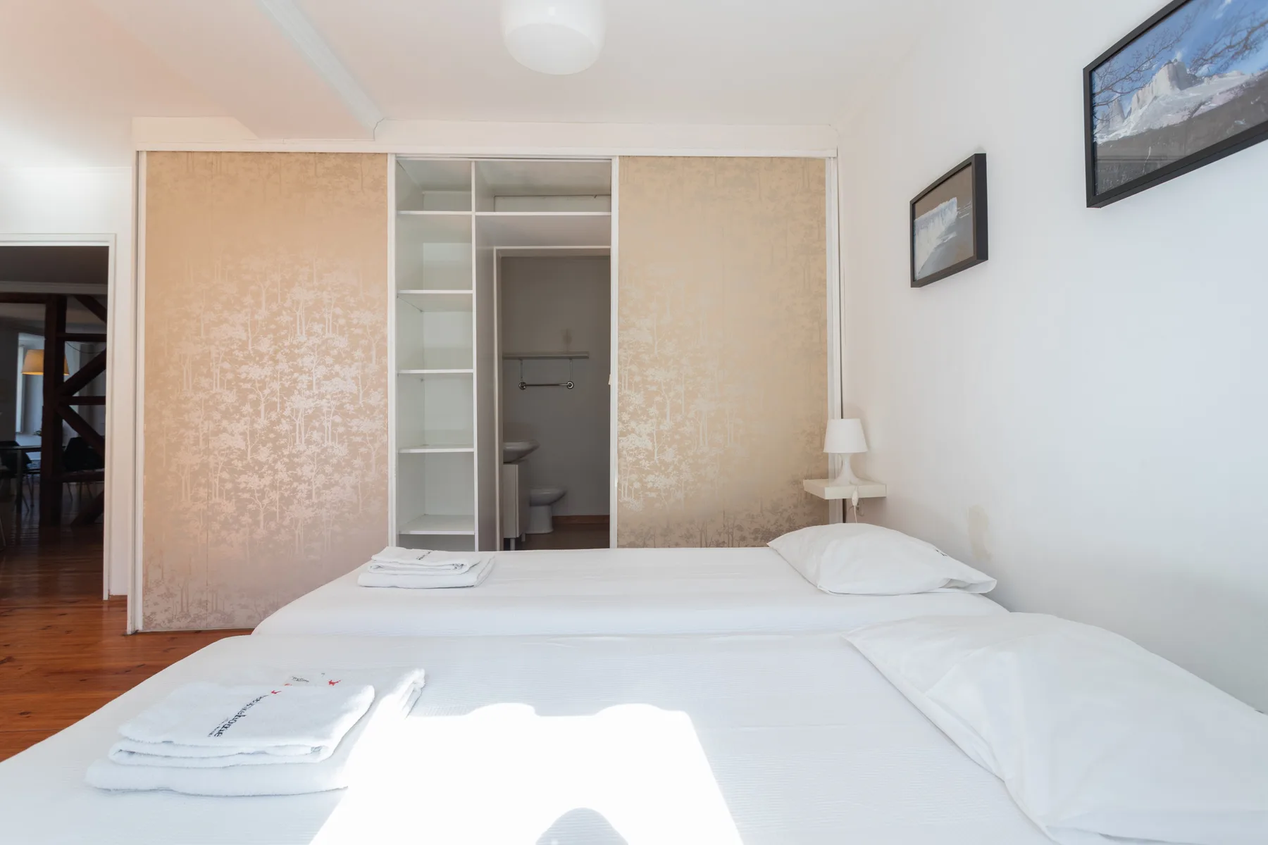 Un dormitorio luminoso con una cama tendida y un armario abierto.