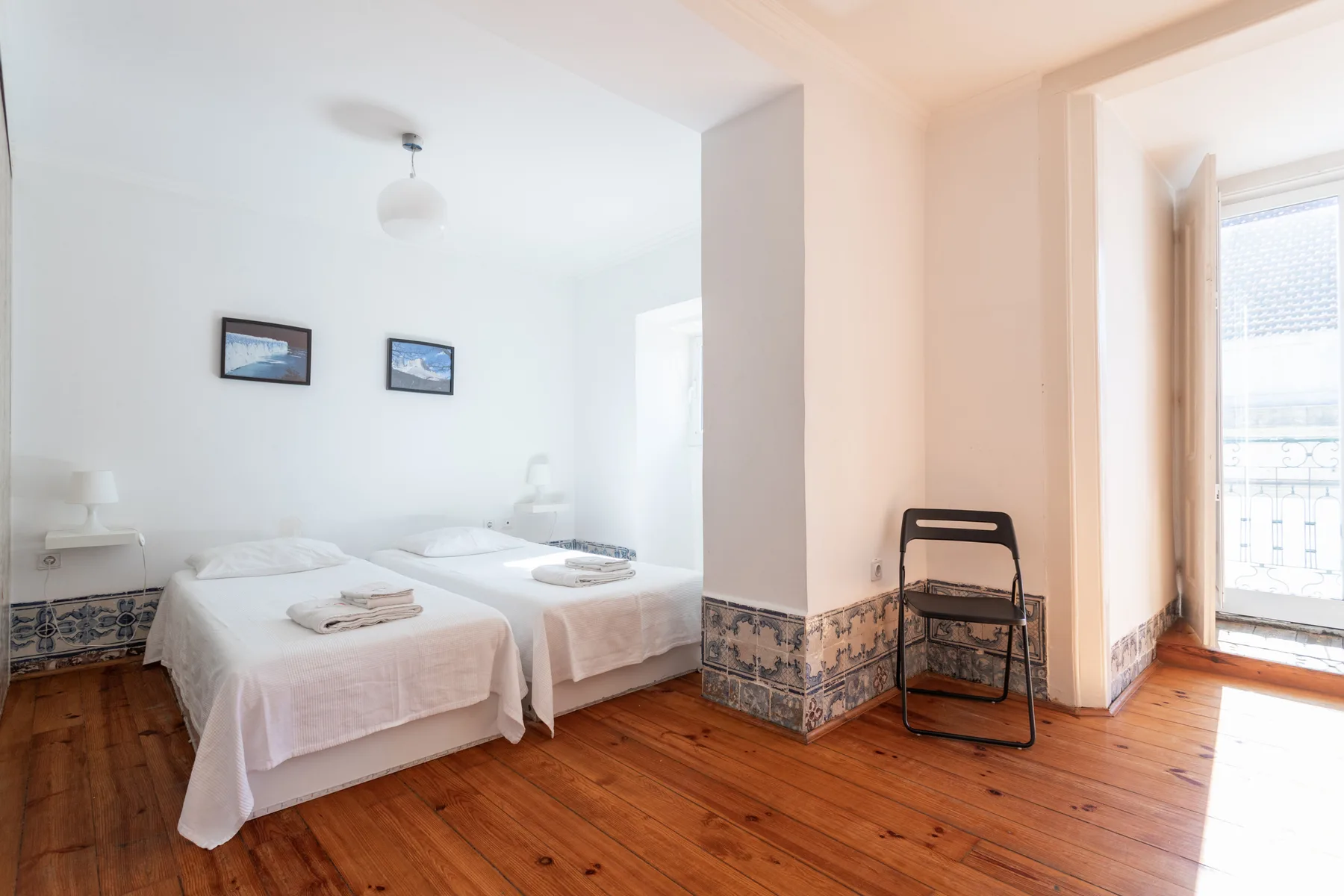 Dormitorio con dos camas y una puerta luminosa que da a un balcón.