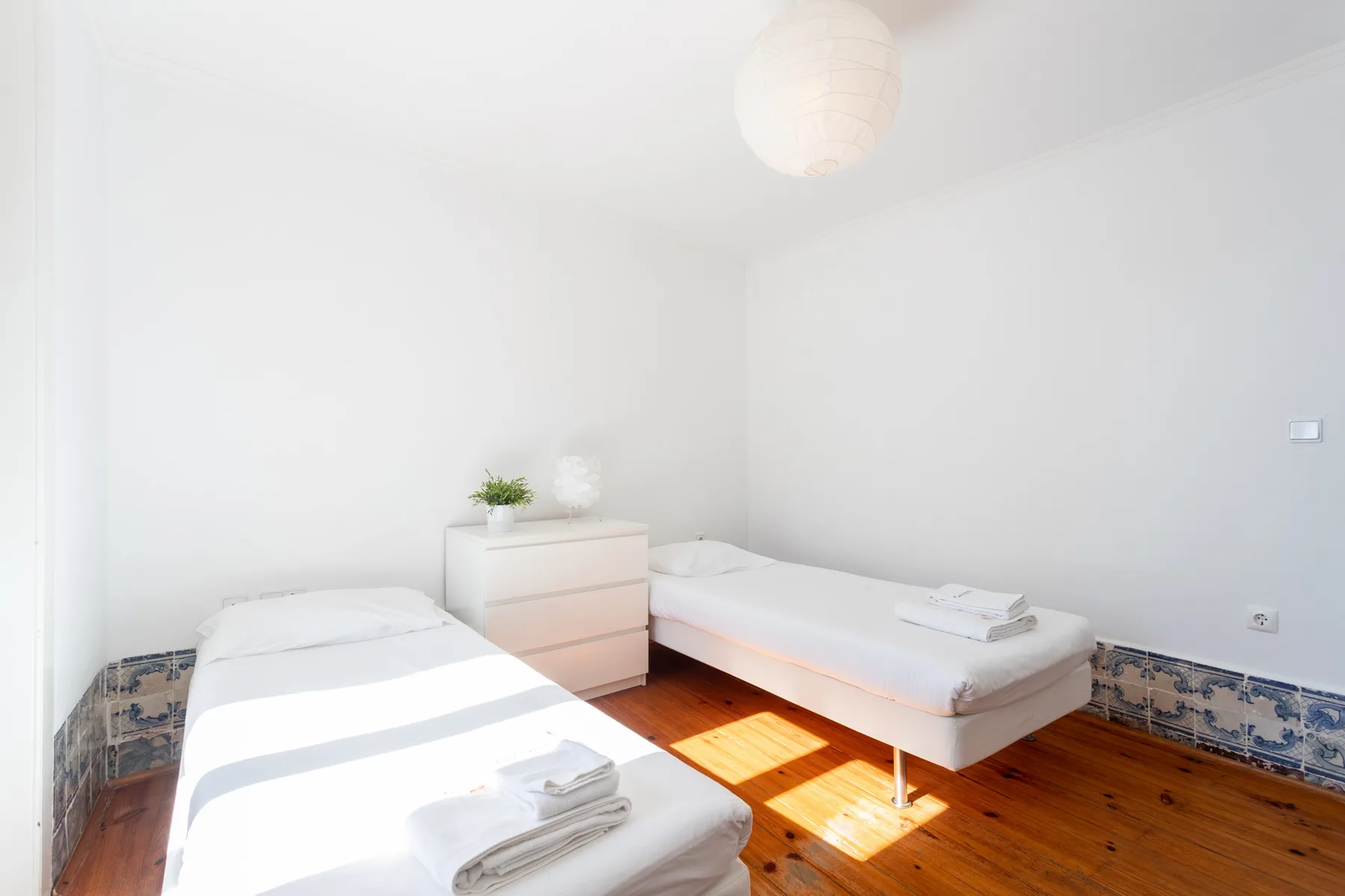Un dormitorio luminoso con dos camas y una pequeña cómoda junto a la cama.