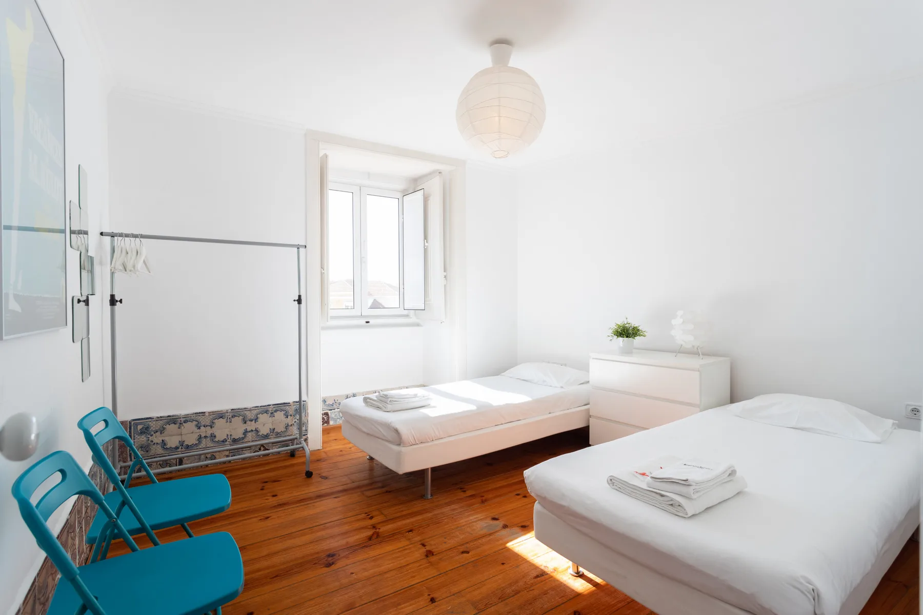 Un dormitorio luminoso con dos camas, asientos turquesa y una ventana.
