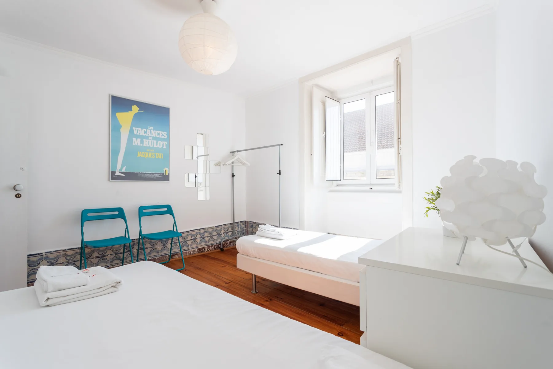 Un dormitorio luminoso con dos camas, asientos turquesa y una ventana.