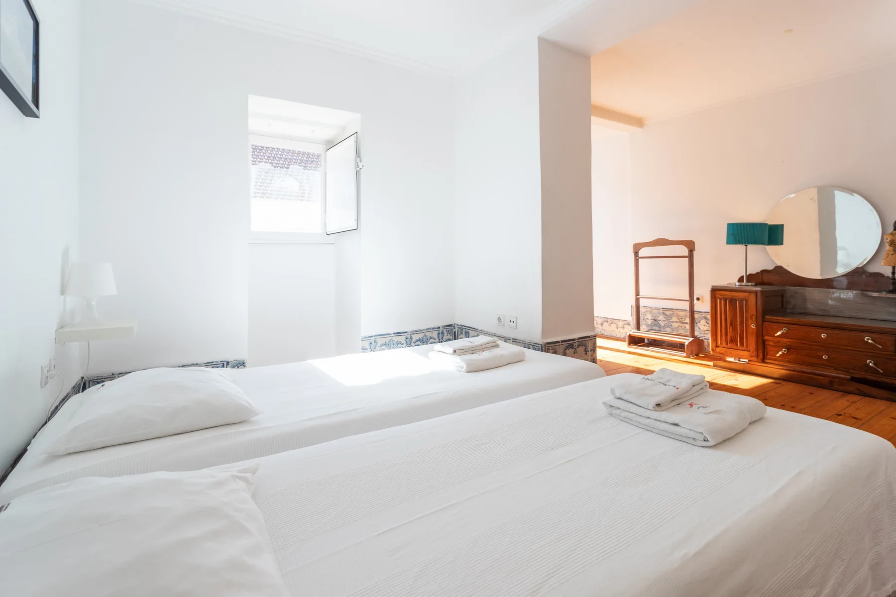 Dormitorio con ropa de cama blanca y una cómoda de madera.