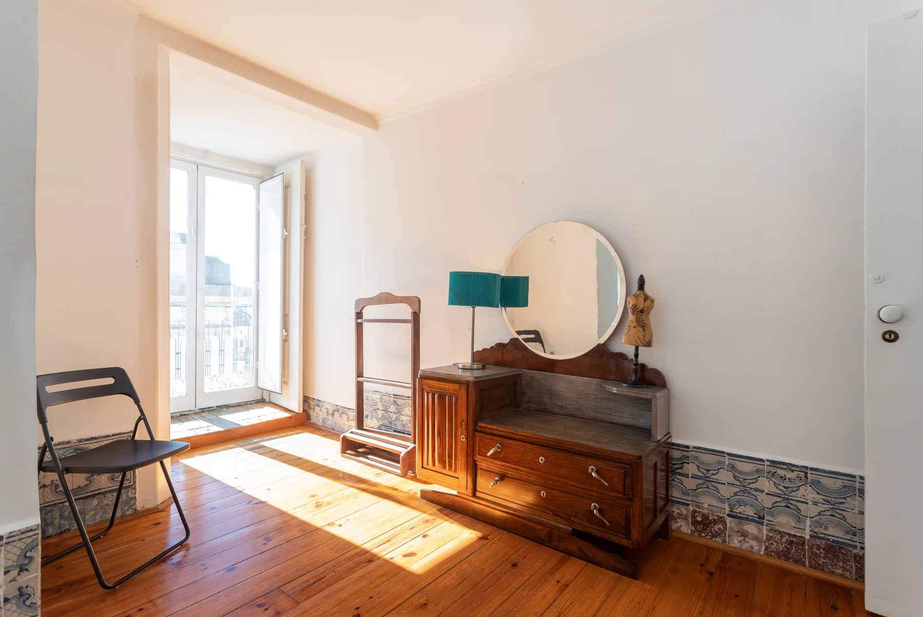 Una habitación soleada con suelo de madera, una cómoda y una puerta abierta al balcón.