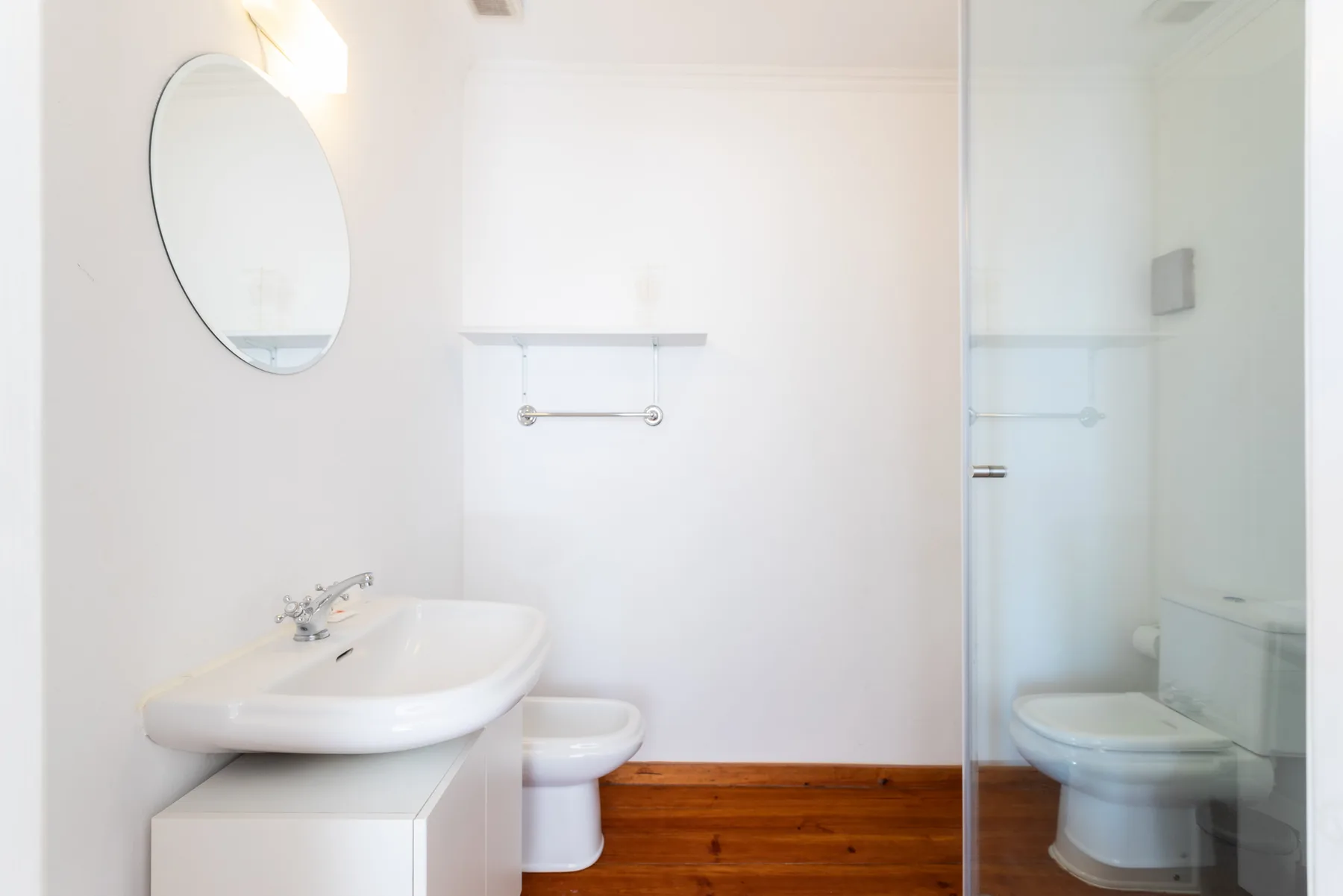 Un baño luminoso con lavabo, espejo y mampara de ducha de vidrio.