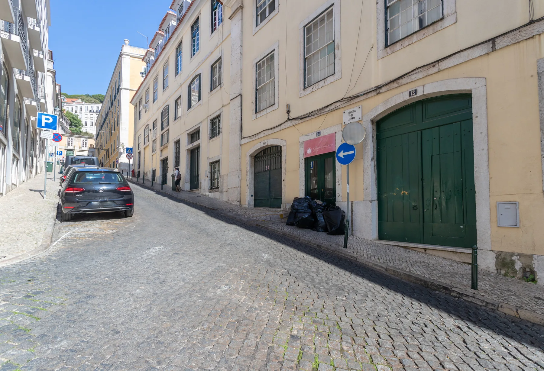 Una calle empedrada pasa junto a edificios claros y coches estacionados.