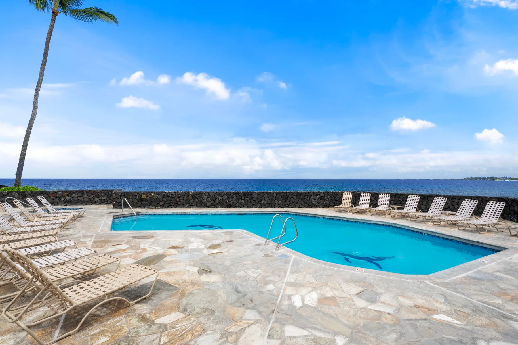 Una piscina junto al mar está rodeada de tumbonas y una terraza pavimentada.
